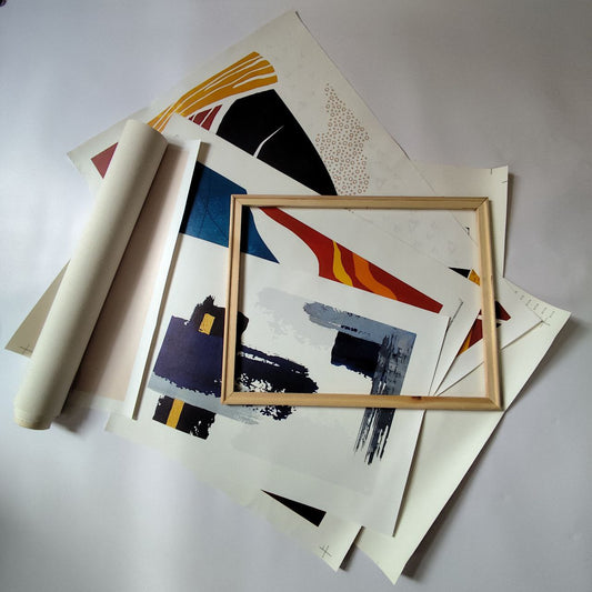 Unframed modern art prints and a wooden stretcher frame lying on a flat surface, showing rolled and flat canvas pieces with colorful abstract designs.