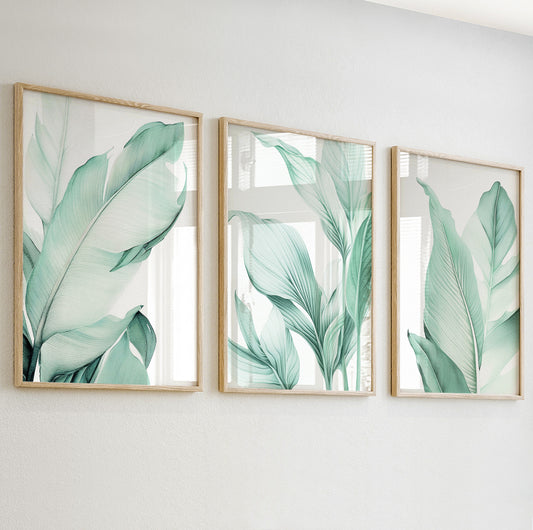 Detailed close-up of a sage green tropical leaf print in a minimalist natural wood frame on a white wall.

